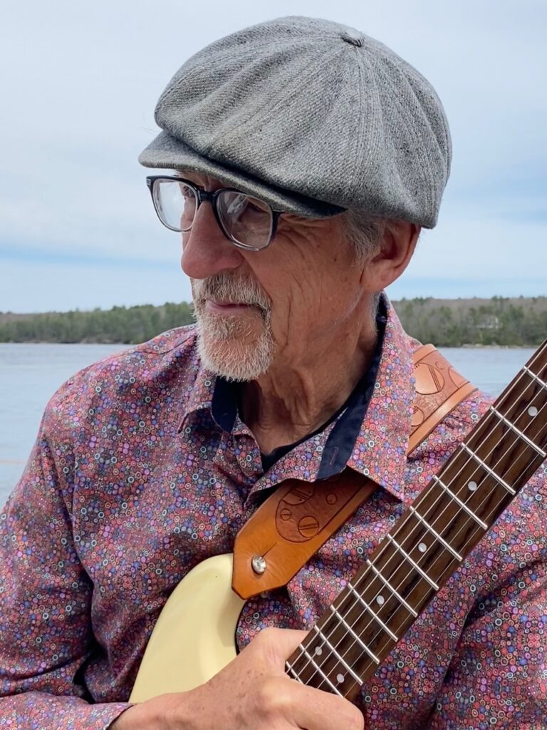 Peter Macdonald Blachly, with guitar, with lake in background