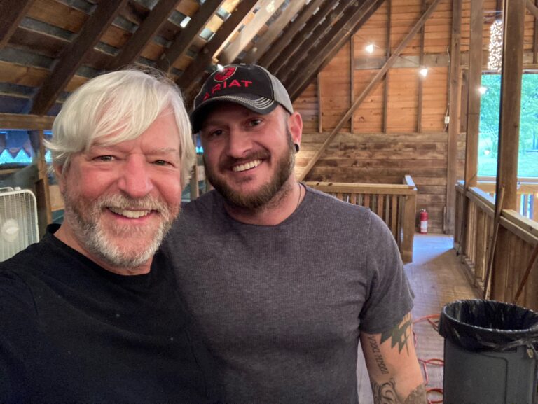 Buddy Mondlock and Wade Bates snapshot. They are in a wood-paneled room and smiling.