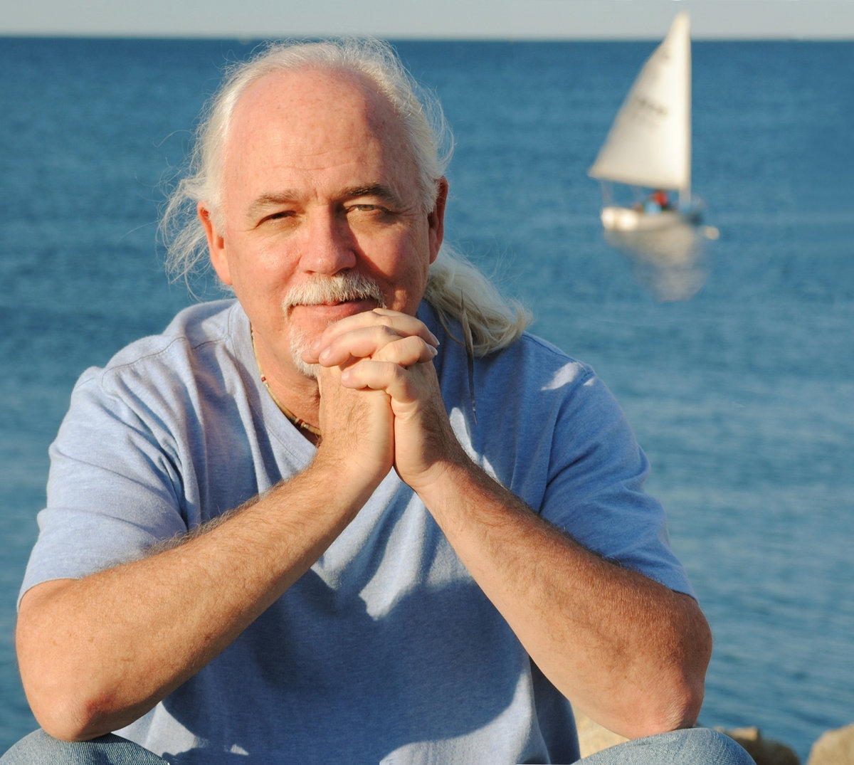 Craig Bickhardt folds hands in front of sailboats